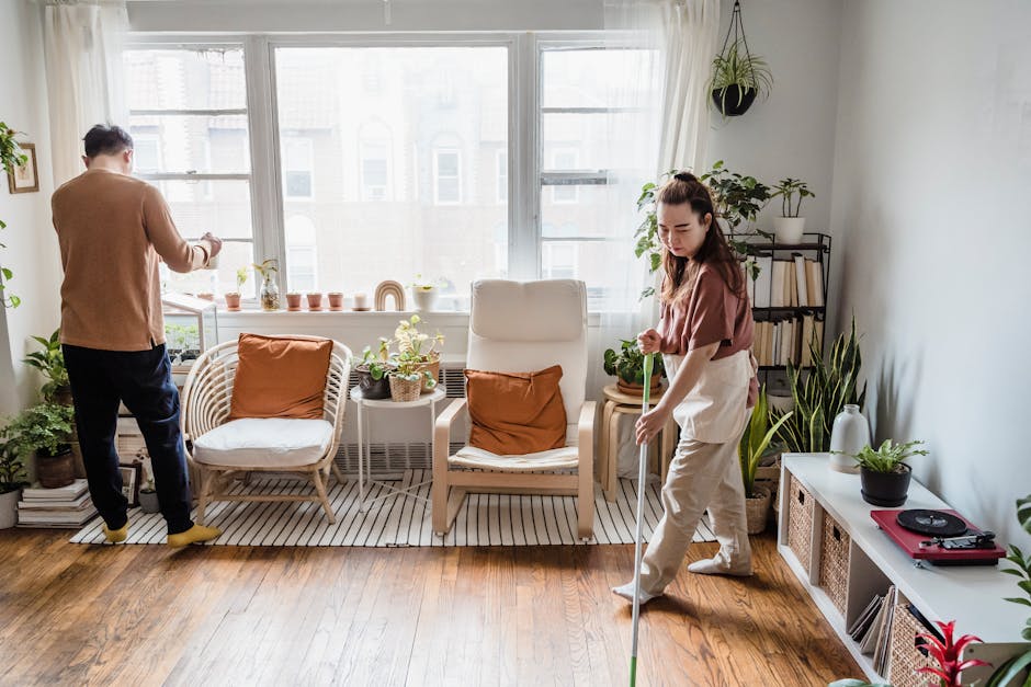 Couple cleaning a bright and cozy living room filled with plants and natural light.