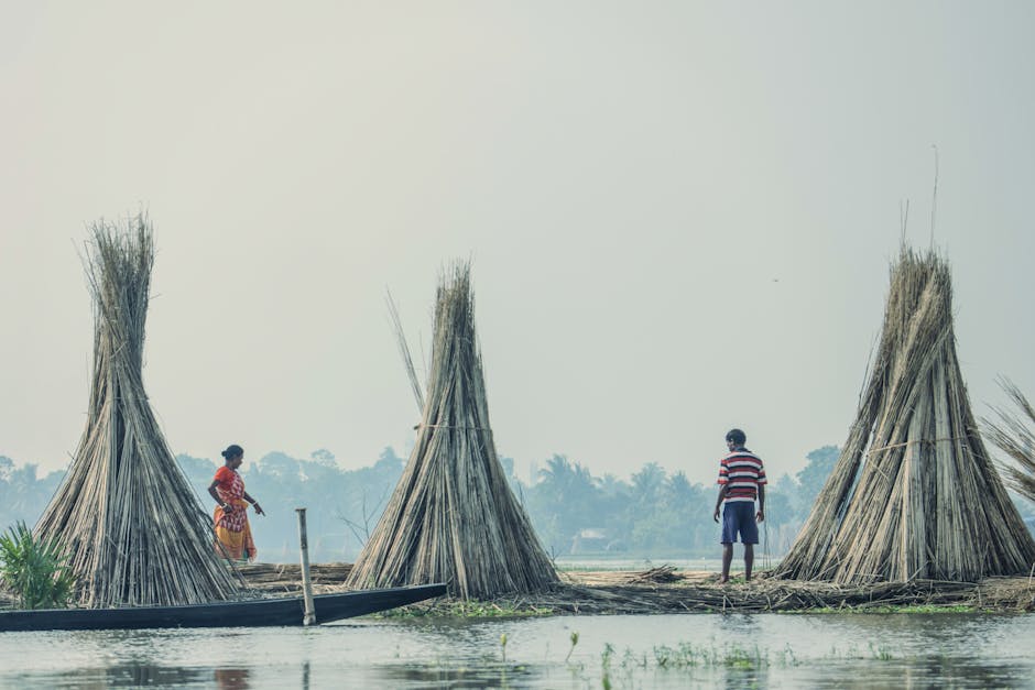 Two people near traditional haystacks by a river, showcasing rural life.