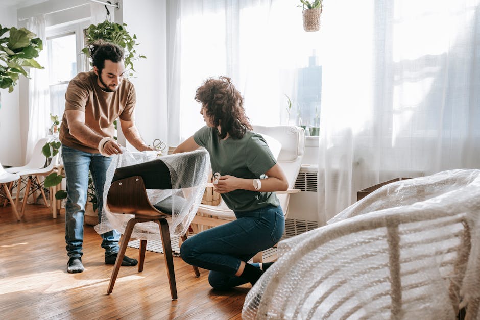 Man and woman wrapping furniture with bubble wrap in a bright room, preparing to move.